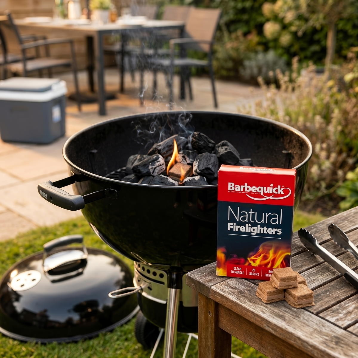 Barbequick natural firelighters box next to a grill with firelighters on a wooden table outdoors.
