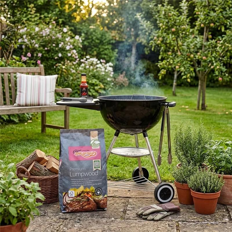 Bag of premium lump wood charcoal next to lit kettle barbeque